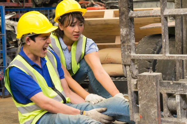 Çalışan bir adamın yakın plan çekiminde kaza, makinistin bacağının üzerinde forklift. Asyalı mühendis, fabrika deposunda ona yardım eden bir forklift ve mühendis kadın tarafından ezildi.