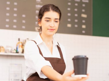 Beyaz tenli güzel baristanın sağ tarafında bir elinde kahve fincanı, diğer elinde de kahve fincanı var. Kahve barında ve yemek servisinde çalışıyor.