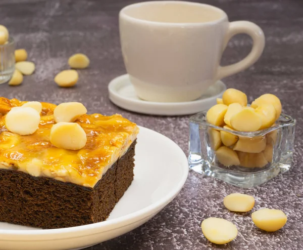 Toffee chocolate cake slice with macadamia seeds in small bowl and coffee cup on stone background for dessert break. Toffee cake made from bake, dark chocolate, macadamia, nut, caramel, and coffee