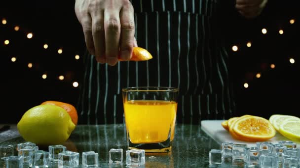 男はテーブルの上のオレンジジュースの上にスライス新鮮なオレンジを絞る バーテンダーはバーでパーティーで飲むためのフルーツカクテルや新鮮なジュースを準備します — ストック動画