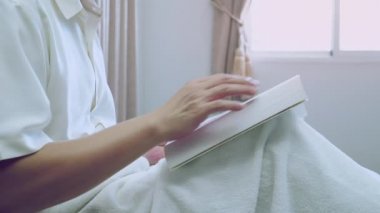 Asyalı adam, sonbahar sabahı dinlenmek için yatak odasındaki pencerenin yanındaki yatakta kitap okudu.