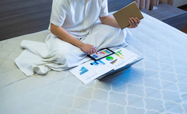 asian business man work online meeting with chart or graph reports on tablet on bed, worker sits and works business on chart or graph for data analytics on bed at home
