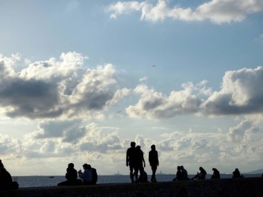 Aydınlık bir Aralık gününde rıhtımda ürperen insan siluetleri, Alimos, Yunanistan