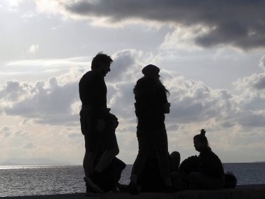 Aydınlık bir Aralık gününde rıhtımda ürperen insan siluetleri, Alimos, Yunanistan