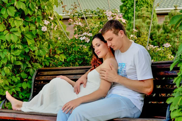 Счастливая беременная пара сидит на скамейке запасных в парке — стоковое фото