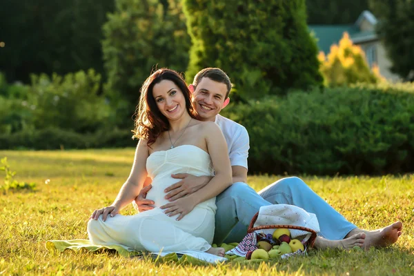 Feliz casal grávida sentado na grama no parque — Fotografia de Stock