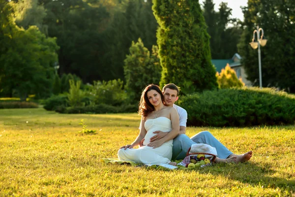Feliz casal grávida sentado na grama no parque — Fotografia de Stock