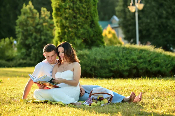 Gelukkige zwangere paar zittend op het gras in park — Stockfoto