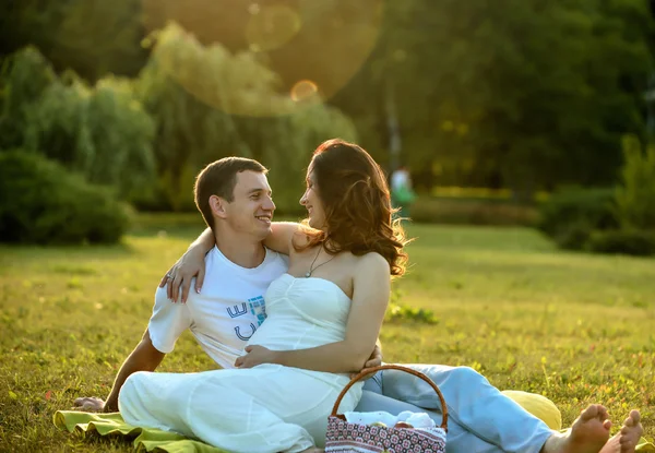 Gelukkige zwangere paar zittend op het gras in park — Stockfoto