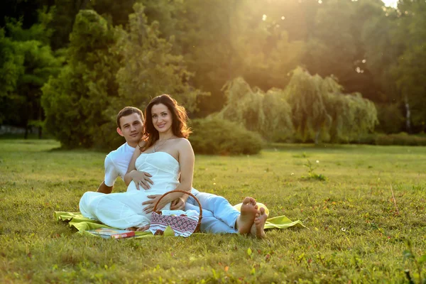 Gelukkige zwangere paar zittend op het gras in park — Stockfoto