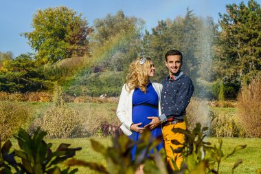 Gökkuşağı arka plan ile genç hamile çift ayakta