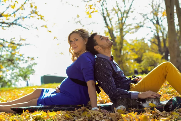 Jovem casal grávida sentado em folhas amarelas no parque — Fotografia de Stock