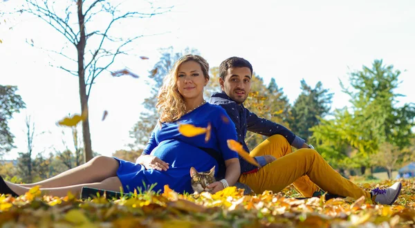 Jovem casal grávida sentado em folhas amarelas no parque — Fotografia de Stock