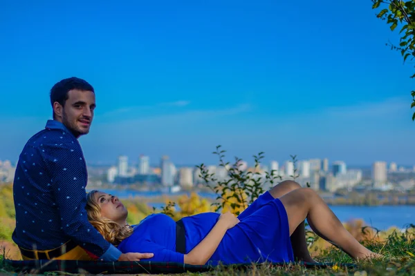 Casal grávida sentado no parque com vista para a cidade — Fotografia de Stock