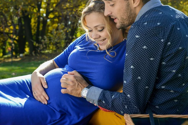 Pais felizes esperando bebê, tocando barriga, sentado na grama verde — Fotografia de Stock
