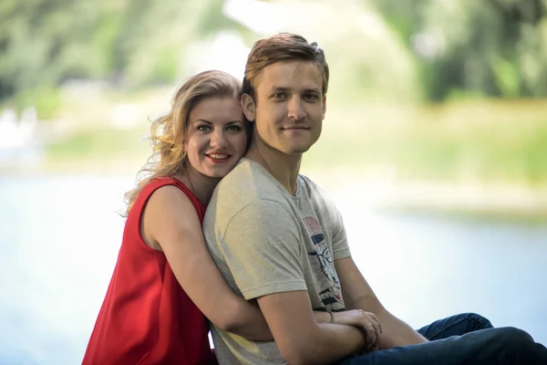 Fiatal és boldog pár ül a padon átölelve. Folyó háttér — Stock Fotó