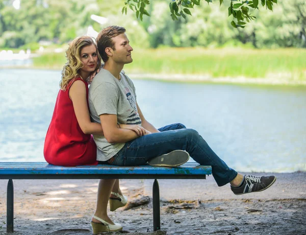 Casal jovem e feliz sentado no banco abraçando. Fundo do rio — Fotografia de Stock