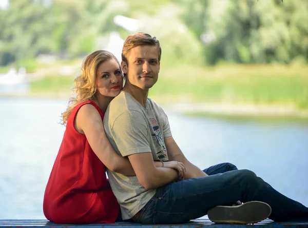 Jong en gelukkige paar zittend op de Bank te knuffelen. Achtergrond van de rivier — Stockfoto