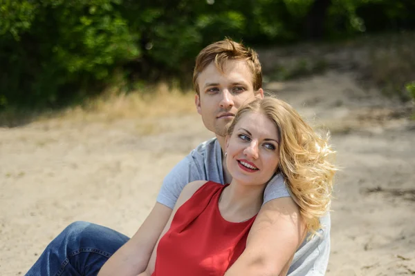 Jovem casal sentado na areia sorrindo e abraçando — Fotografia de Stock