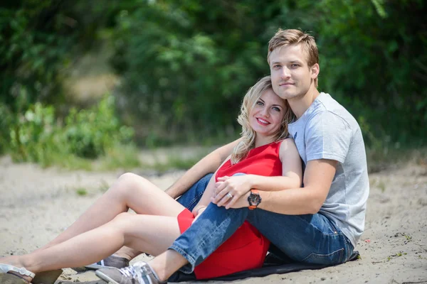 Jong koppel zit op het zand, glimlachend en knuffelen — Stockfoto