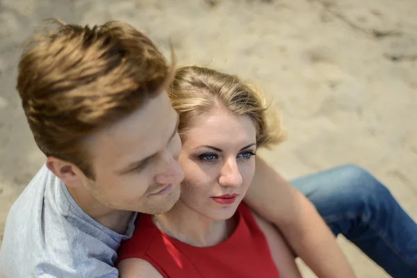 Fiatal pár ül a homokba, és mosolyogva, átölelve — Stock Fotó