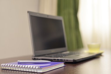 Laptop bir adres defteri, kupa ve kalem masada.