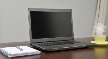 Laptop bir adres defteri, kupa ve kalem masada.