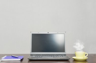 Laptop bir adres defteri, kupa ve kalem masada.