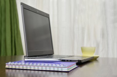 Laptop bir adres defteri, kupa ve kalem masada.