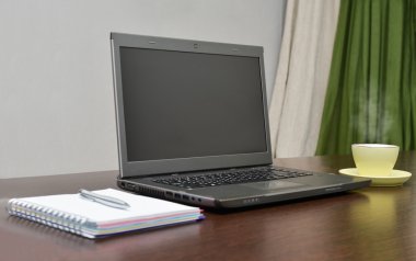 Laptop bir adres defteri, kupa ve kalem masada.