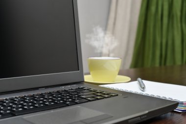 Laptop bir adres defteri, kupa ve kalem masada.