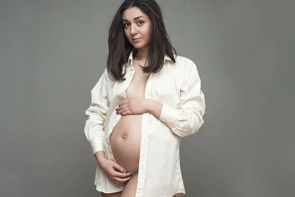 Молодая беременная женщина в белой рубашке держит руки на животе — стоковое фото