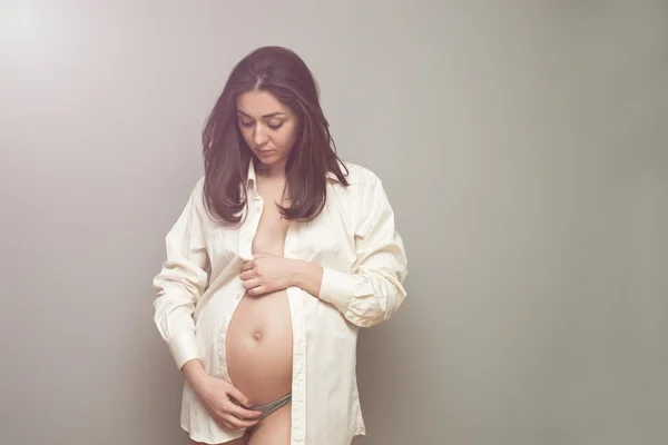 Giovane donna incinta in camicia bianca che tiene le mani sulla pancia — Foto Stock