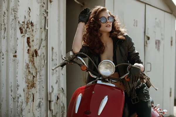Портрет красивой девушки в кожаной куртке, бюстгальтере и очках возле красного мотоцикла — стоковое фото