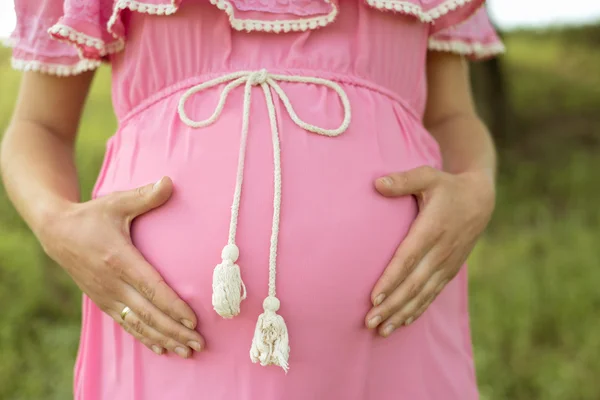 Kobieta w ciąży w różowej sukience, trzymając jej brzuch — Zdjęcie stockowe