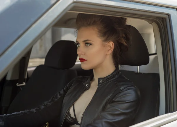 Sexy young girl driving car in leather jacket — Stok fotoğraf