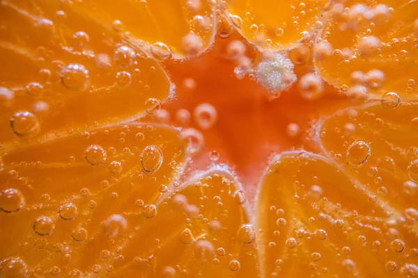 Detail of orange slice in sparkling water. Fresh lemon slice in water with bubbles on sky background.