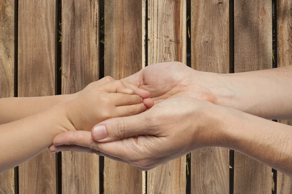 Padre e hijo tomados de la mano sobre fondo de madera —  Fotos de Stock