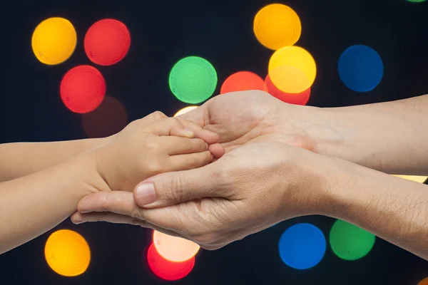 Otec a syn drží za ruce na vánoční osvětlení pozadí. — Stock fotografie
