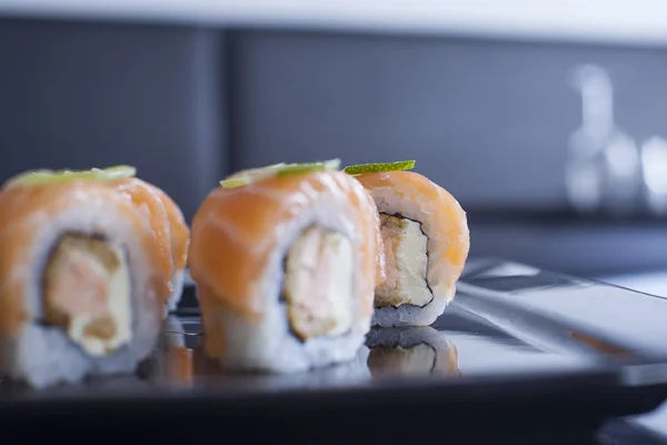 Rolo de sushi com queijo creme e salmão frito. Coberto com salmão cru e limão . — Fotografia de Stock