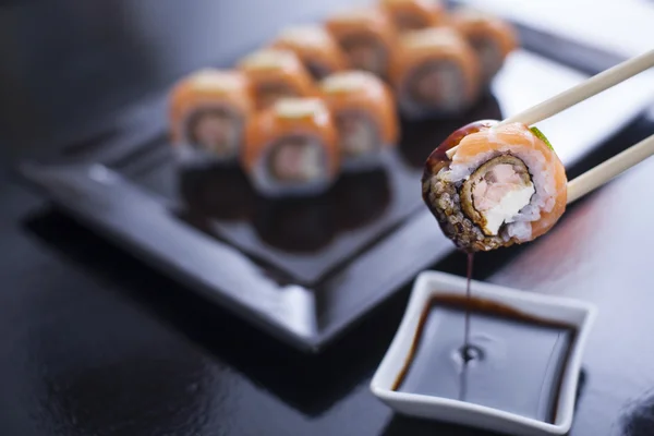 Sushi roll tuorejuustolla ja paistettua lohta. Raakaa lohta ja limettiä. Haetaan syömäpuikoilla soijakastikkeesta. . — kuvapankkivalokuva