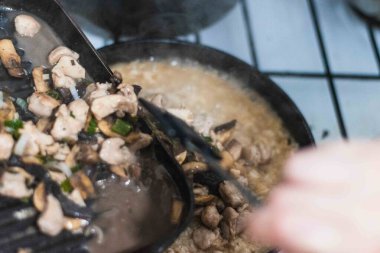 Orta yaşlı bir kadının eli silikon uçlu ızgara olmayan çatal kullanarak ev yapımı tavuk ve mantarlı risotto hazırlıyor.