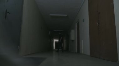 Siyah elbiseli ve siyah şapkalı bir adam karanlık bir koridorda duruyor.