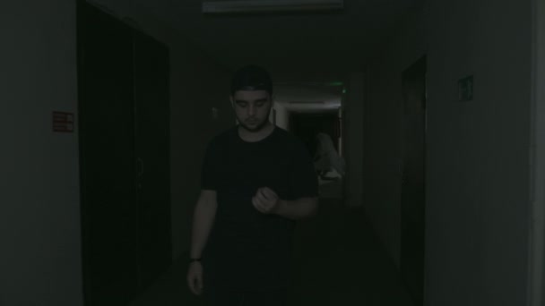 A guy in black clothes and a black velvet walks down the dark corridor — Vídeo de Stock