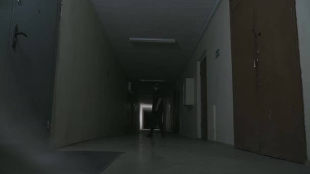 Ένας τύπος με μαύρα ρούχα και μαύρο καπέλο στέκεται σε ένα σκοτεινό διάδρομο. — Αρχείο Βίντεο
