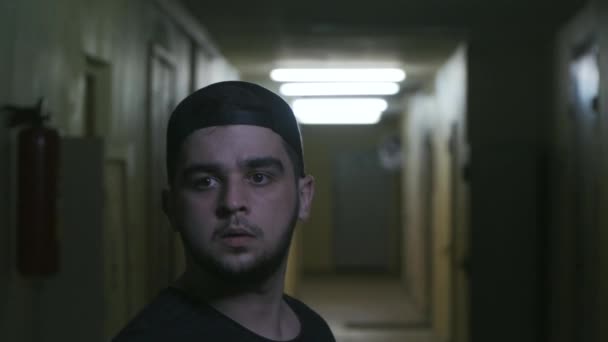 Молодой парень в черной кепке поворачивается, чтобы шуметь в темном коридоре — стоковое видео