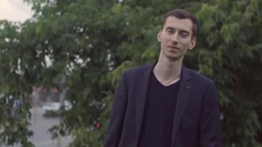 Ceketli genç bir adam bardak tutuyor ve dans ediyor.