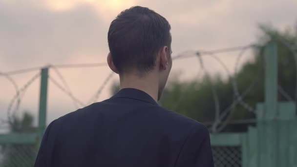 A young guy in a jacket looks over the fence — Vídeo de Stock