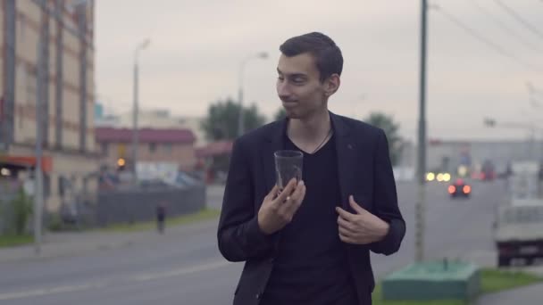 Un joven con chaqueta sostiene un vaso y baila — Vídeo de stock