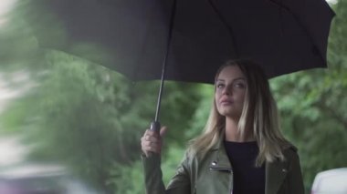 Genç Avrupalı bir kız elinde siyah bir şemsiyeyle duruyor.